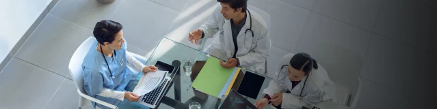Fünf Ärzte sitzen um einen Glastisch während eines Meetings.